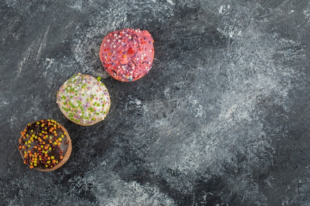 Three colorful sweet doughnuts with sprinkles .