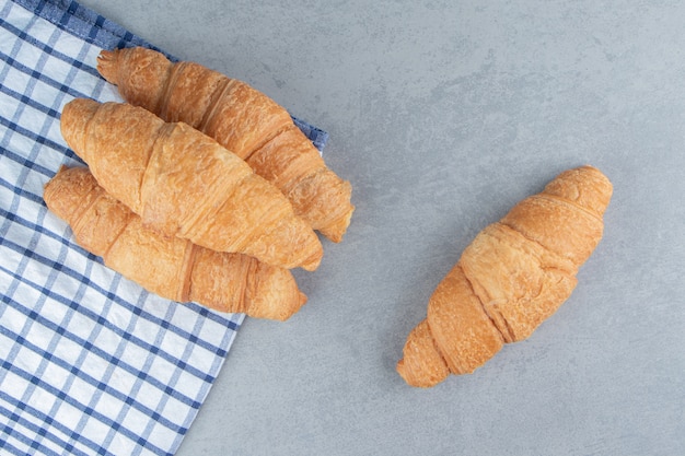 Three croissants stacked on the towel with a croissant on the marble background. High quality photo