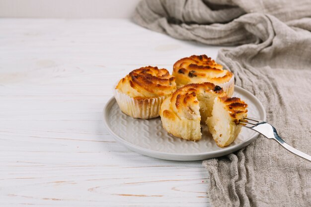 Three cupcakes on plate with fork over wooden backdrop