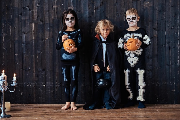 Foto gratuita tre bambini carini in costumi spaventosi durante la festa di halloween in una vecchia casa. concetto di halloween.