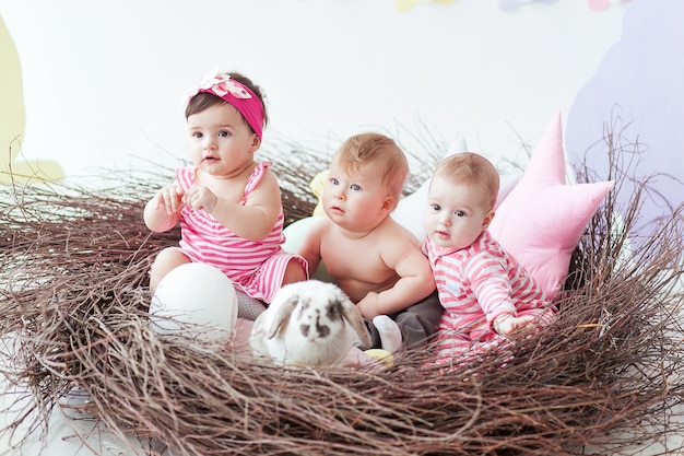 Tre simpatici piccoli bambini e coniglio con uova di pasqua seduto nel grande nido