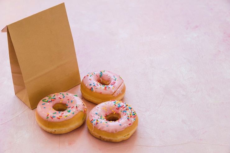 Free Photo three delicious donuts with parcel on pink background