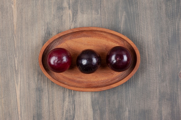 Foto gratuita tre deliziose prugne su un piatto di legno. foto di alta qualità