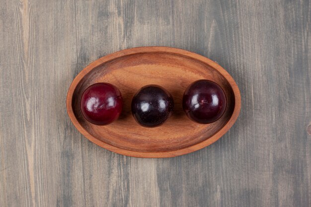 Three delicious plums on a wooden plate. High quality photo