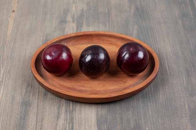 Three delicious plums on a wooden plate. High quality photo