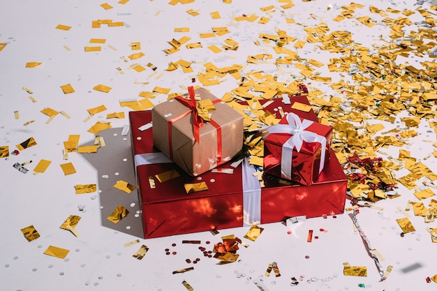 Три рождественских подарка разного размера, завернутые в оберточную бумагу, с бантом и россыпью золотых конфетти.