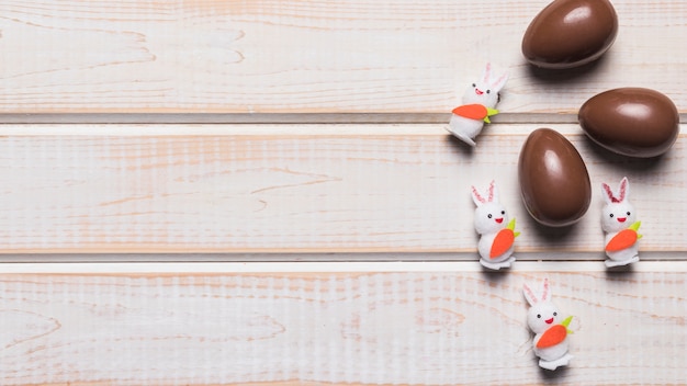 Three easter white rabbits and chocolate eggs on wooden desk