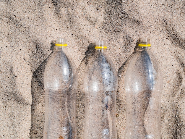 Tre bottiglie di plastica vuote dispongono in fila sulla sabbia