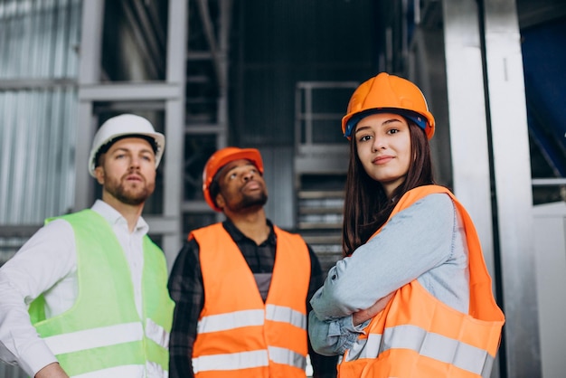 Three factory workers in safety hats discussing manufacture plan