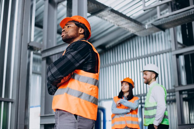 Three factory workers in safety hats discussing manufacture plan