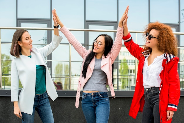 Three fashionable female friends giving high five at outdoors