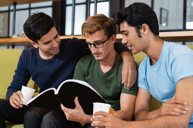 Three fellow students reading textbook and drinking coffee