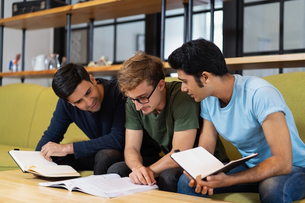 Free photo three fellow students reading textbook and preparing for exam