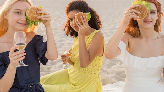 ビーチでハンバーガーを一緒に楽しむ3人の女性の友人
