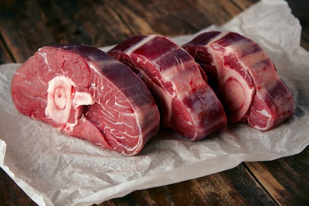 Три стейка из свежего мяса с косточкой из белой крафт-бумаги на деревянном столе