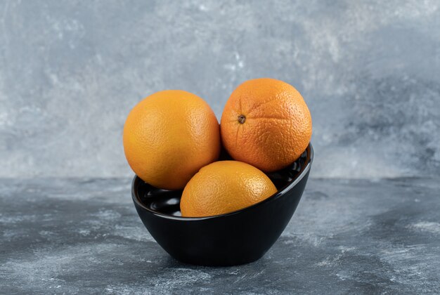 Three fresh oranges in black bowl.