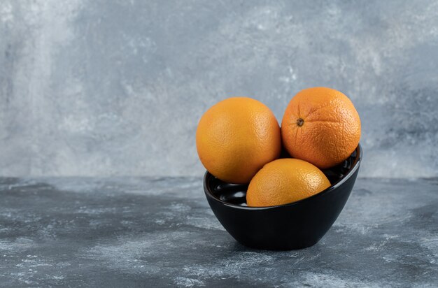 Three fresh oranges in black bowl. 