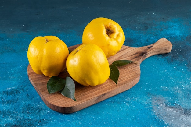 Three fresh quince fruits with leaves placed on a wooden cutting board