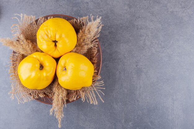 Three fresh quince fruits with wheat ears placed on stone table.