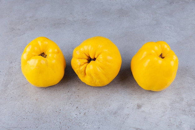 Three fresh quince fruits with wheat ears placed on stone table.