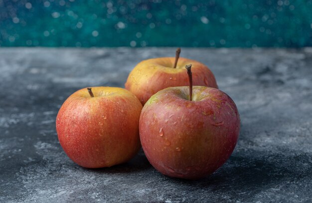 Three fresh red apples on a marble background.