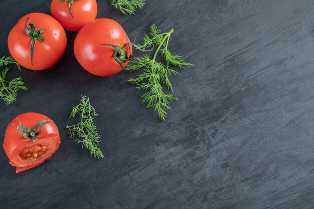 Three fresh tomatoes with leaves on a dark background. 