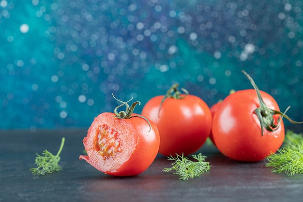 Three fresh tomatoes with leaves on a dark surface.