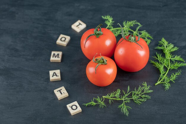 Three fresh tomatoes with leaves on a dark surface.