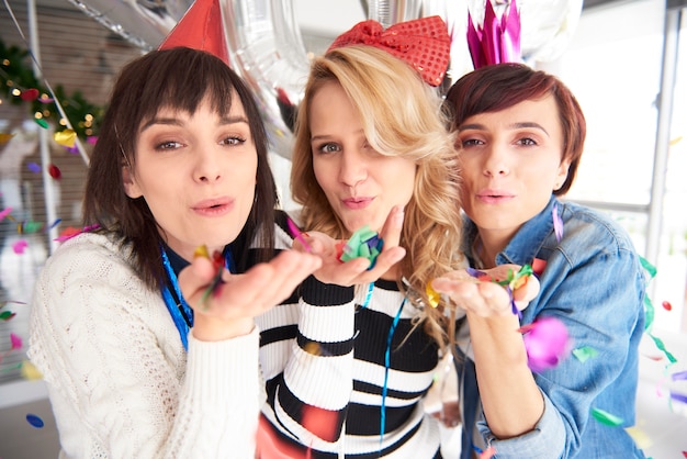 Three friends blowing some confetti