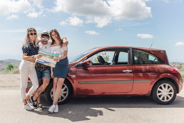 Three friends holding map standing near the modern car on road