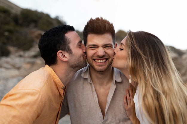 Three friends kissing while posing together during a beach party