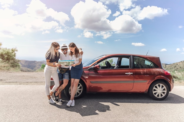 Three friends looking at map standing near the modern car on road