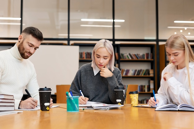 Three friends studying from documents and notebooks in a library