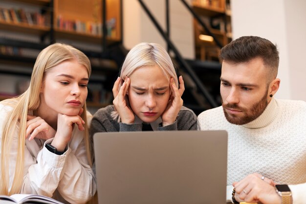 ノートパソコンを使用して図書館で勉強している3人の友人