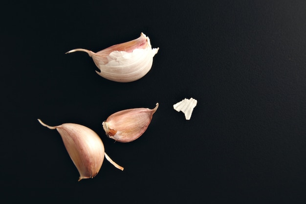 Three garlic cloves and some dry peel on a smooth black background