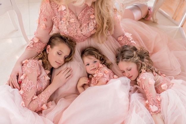 Три девушки в розовых платьях спят на коленях мамы