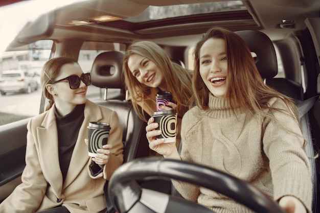 Three girls sitting inside the car and drinking a coffee