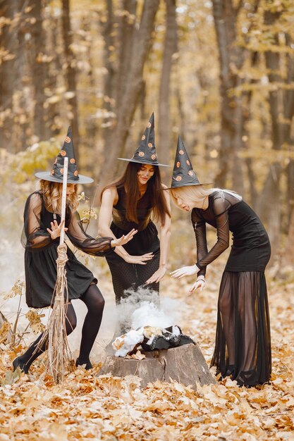Three girls witches in forest on Halloween. Girls wearing black dresses and cone hats. Witches make a magic potion.