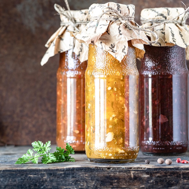 Free photo three glass bottles of assorted georgian tkemali sauce with ingredients on rustic wooden table