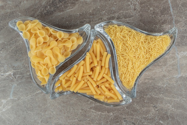 Three glass bowls of raw pasta on marble surface