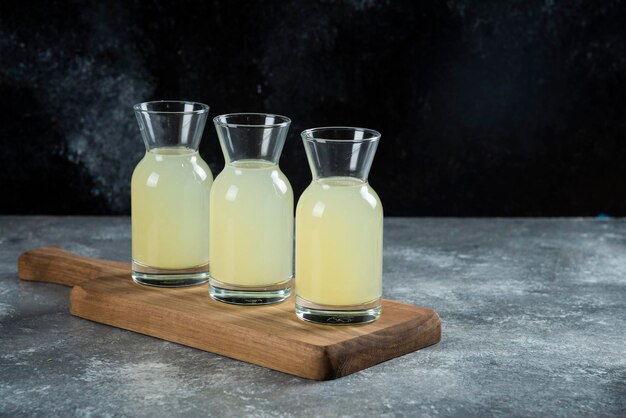 Three glass jugs of fresh lemon juice on wooden board