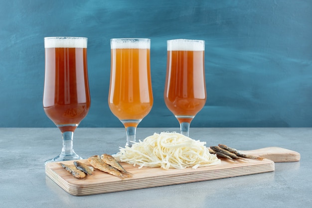 Three glasses of beer with fish and cheese on wooden cutting board . High quality photo