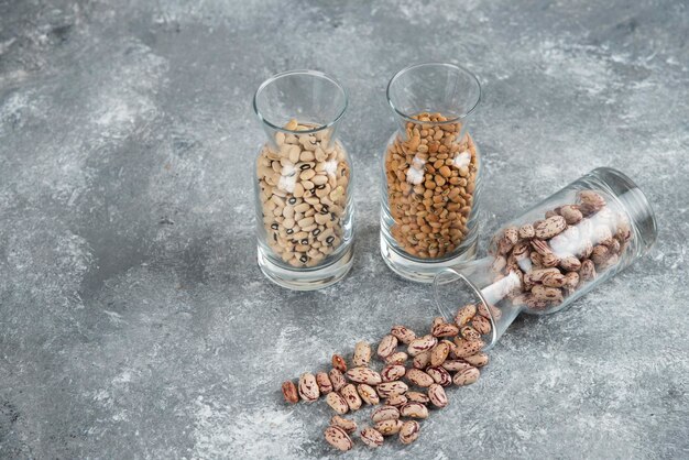 Three glasses of jar with unprepared beans on a gray table.