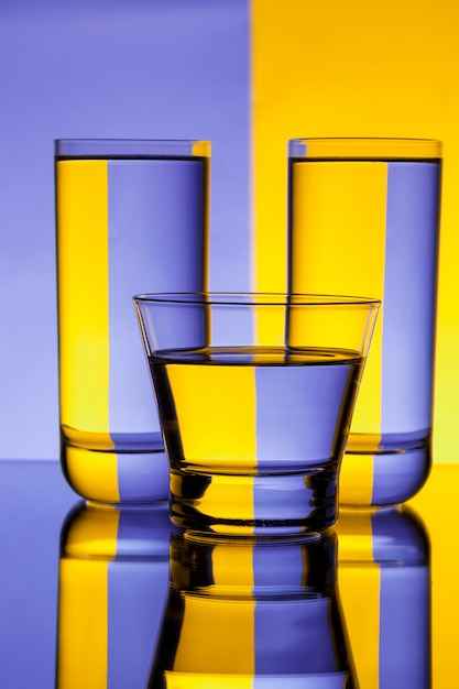 Three glasses with water over purple and yellow wall