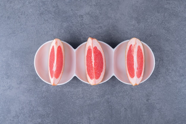 Three grapefruit slices on grey background.