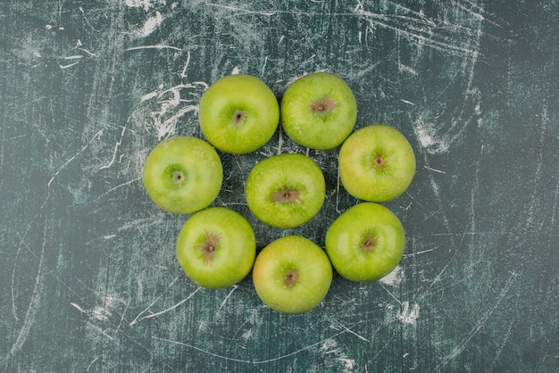 Three green apples on marble surface.