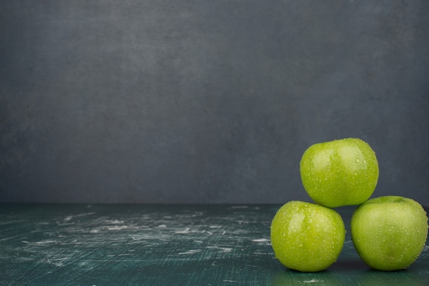 Foto gratuita tre mele verdi sulla superficie di marmo.