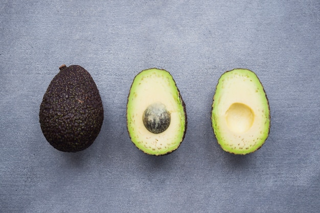 Three green avocados on grey table