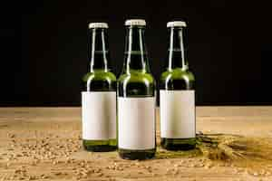 Free photo three green beer bottles with ears of wheat on wooden surface