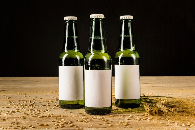 Three green beer bottles with ears of wheat on wooden surface